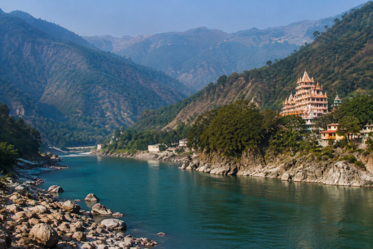 Turquoise river winds through rocky banks with forested mountains and a multi-tiered pagoda on the right hillside.