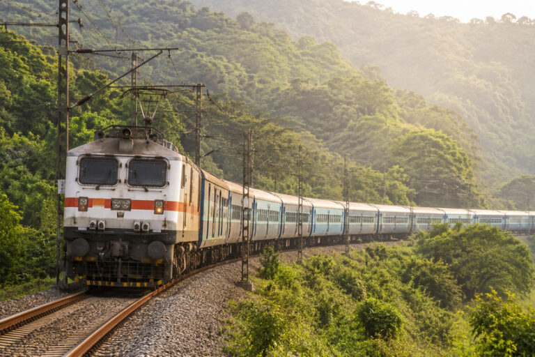 Passenger train curving along a single-track railway through a forested hillside.