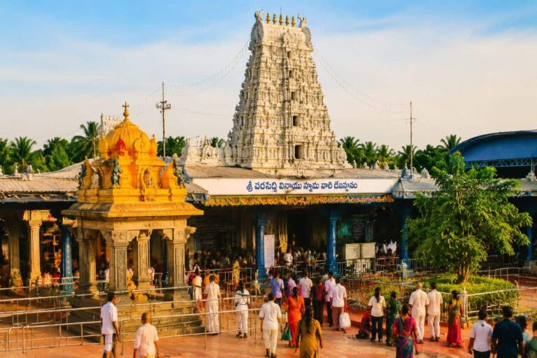 Hindu temple complex with a tall white gopuram and golden shrine, crowded with visitors outside on a sunny day.