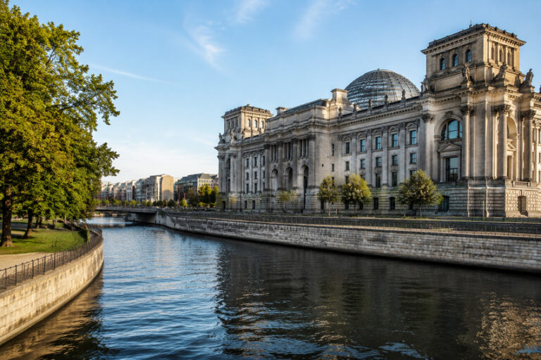 Reichstag building in Berlin along the Spree River with a glass dome and trees lining the bank.