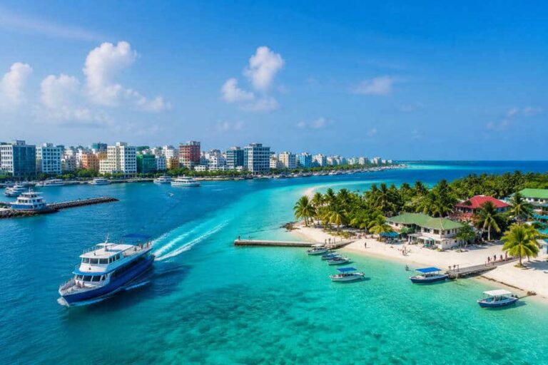 Turquoise tropical bay with a boat cruising past a palm-fringed beach and a cityscape in the distance.