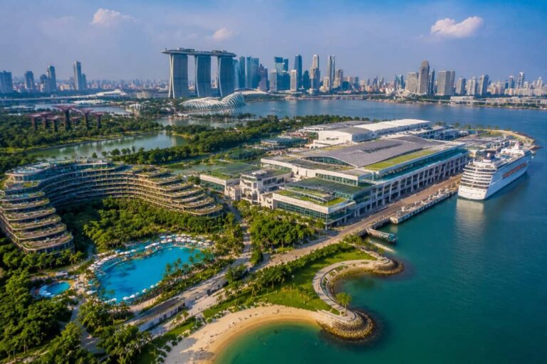 Aerial view of Singapore’s Marina Bay area showing Marina Bay Sands, ArtScience Museum, waterway, and a cruise ship docked at the pier with surrounding greenery and city skyline.