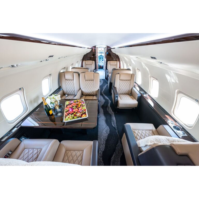 Luxurious private jet cabin with beige leather seats, a wood table, and a fruit platter with champagne.