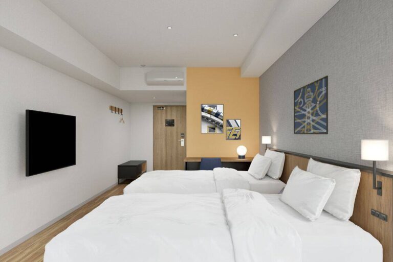 Hotel room with two double beds, wall-mounted TV, and a desk against an orange accent wall.