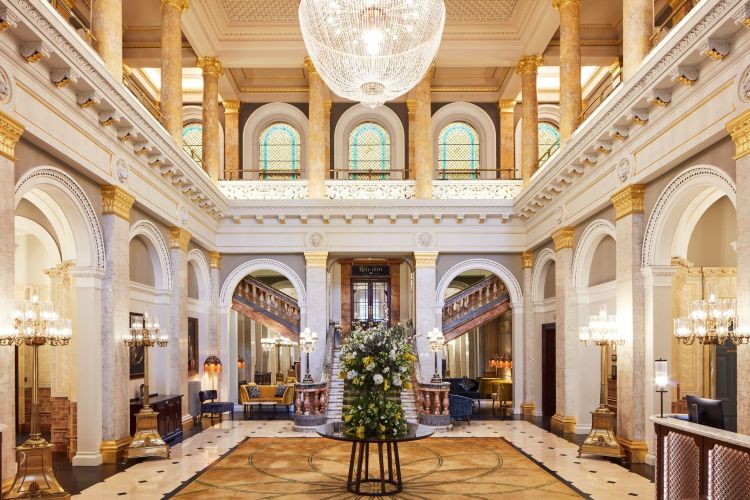 Grand hotel lobby with marble arches, a crystal chandelier, and a central flower arrangement on a round pedestal.