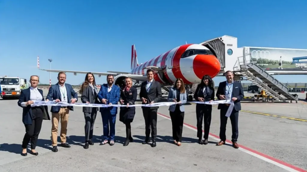 Group of businesspeople cutting a ribbon in front of a red-and-white airplane on a tarmac, celebrating a launch event.