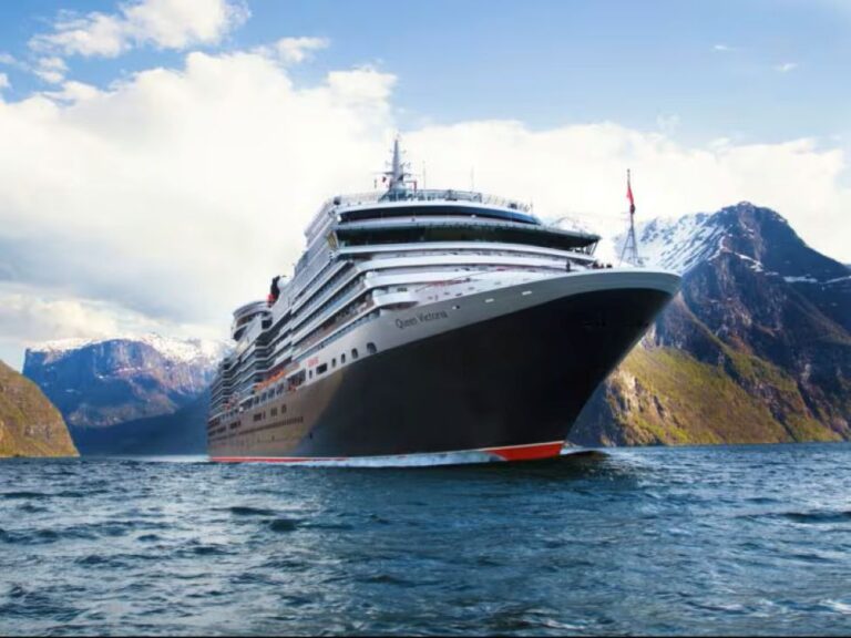 Cruise ship cutting through blue water with snow-capped mountains in the background.
