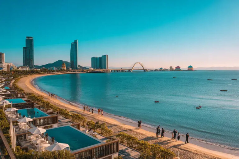 Coastal city beach with blue water, skyline, and arched bridge in the background.
