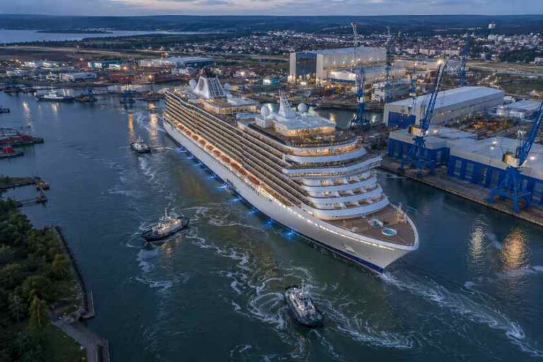 Large white cruise ship docked at a busy harbor with cranes and industrial buildings at dusk.