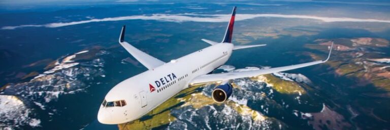 Delta airplane soaring above snow-capped mountains and lakes seen from a high altitude.