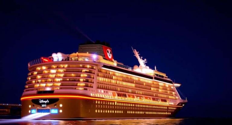 Night view of a Disney cruise ship illuminated at port with multiple decks lit up at night