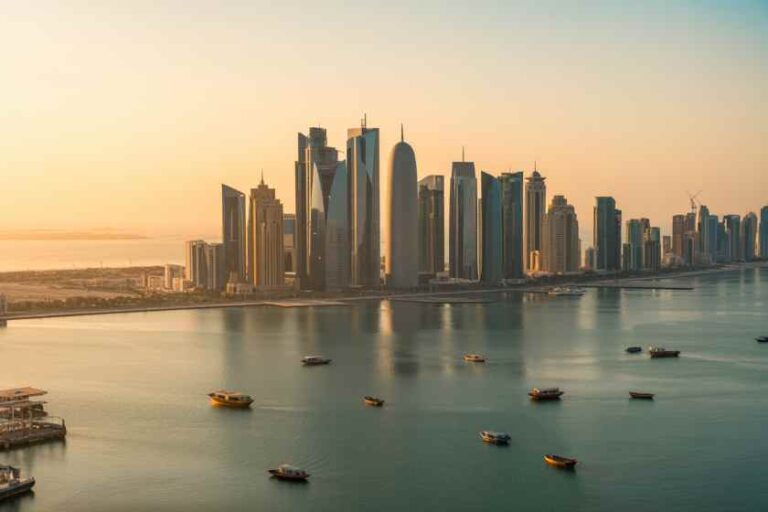 Sunset over a modern city skyline along a calm harbor, with tall glass skyscrapers reflecting on the water and small boats dotting the bay.