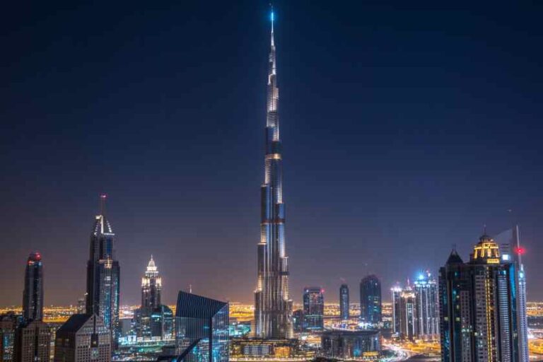 Burj Khalifa towering above Dubai skyline at night, illuminated skyscrapers surrounding it.
