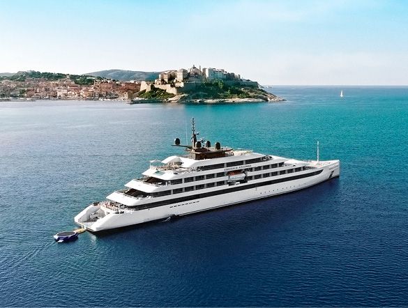 Large white luxury yacht anchored in deep blue water near a coastal town with a hilltop fortress in the background Sailing
