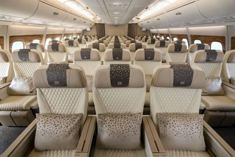Inside an empty airplane cabin with cream quilted seats and beige headrests, arranged in rows along both sides of the aisle.