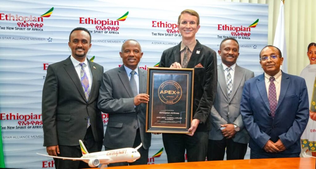 Group of six men in suits posing with a framed award plaque at an Ethiopian Airlines event, a model airplane on the table in front of them.