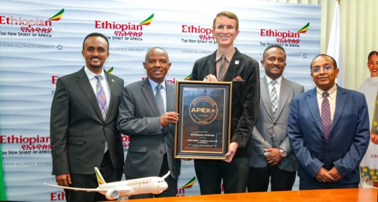 Group of six men in suits posing with a framed award plaque at an Ethiopian Airlines event, a model airplane on the table in front of them.