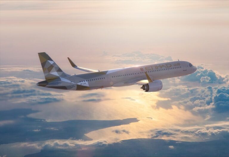 Etihad Airways plane flying above clouds at sunset, wings and engine visible amid a golden sky