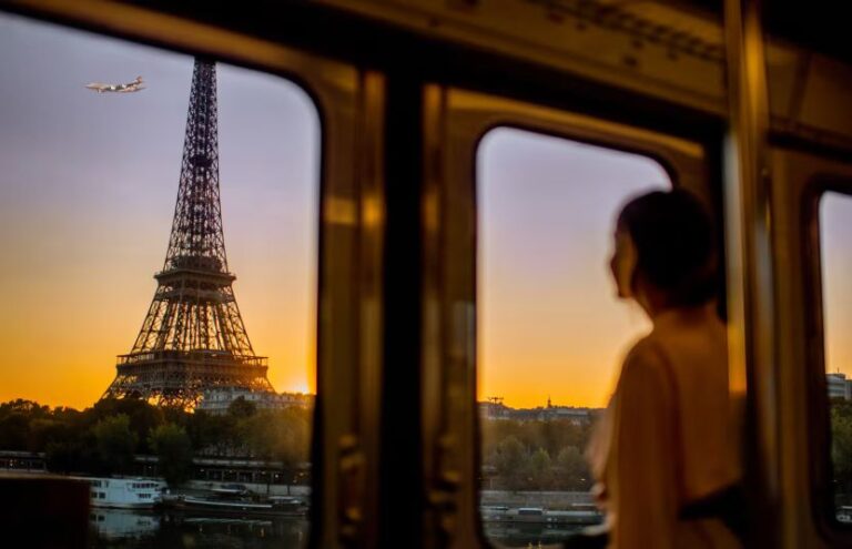 Sunset over the Eiffel Tower viewed from a moving train, with a blurred passenger inside the carriage.