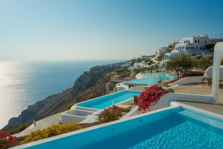 White-washed buildings and turquoise pools cascade down a cliffside toward the blue Aegean Sea.