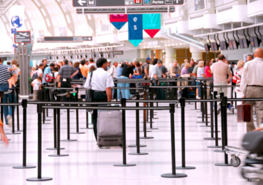 Crowded airport check-in area with passengers queuing and a rolling suitcase in the foreground.