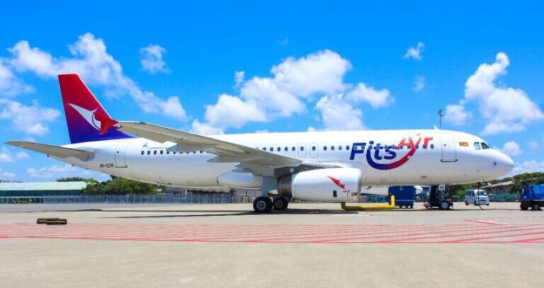 White passenger jet parked on the tarmac with a blue sky above and a red-tailed logo on the tailfin.