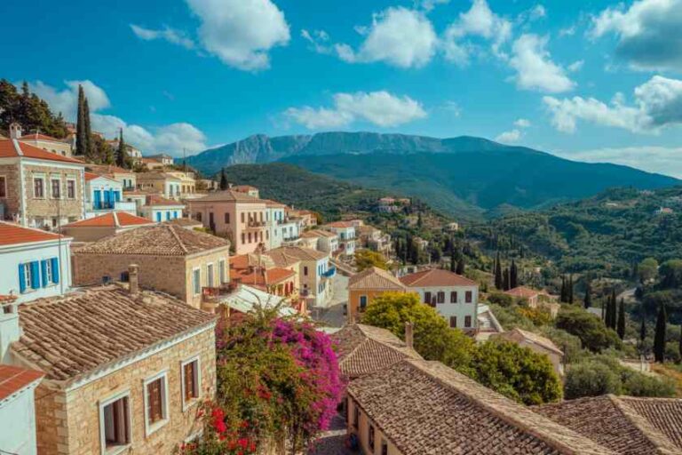 Colorful hillside village with terracotta roofs, blooming bougainvillea, and mountains under a blue sky.