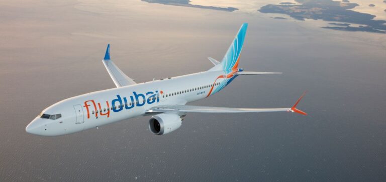 Flydubai passenger jet flying over a calm sea with orange wingtip accents visible in the distance