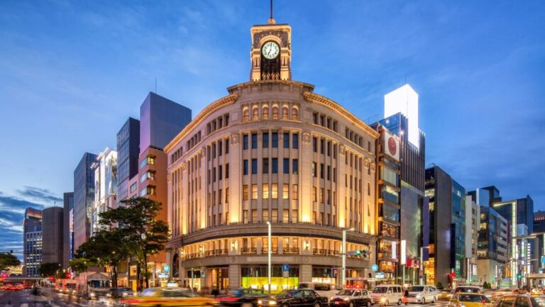 Ginza's Wako building with clock tower lit at dusk, surrounded by shops and traffic on a busy street.