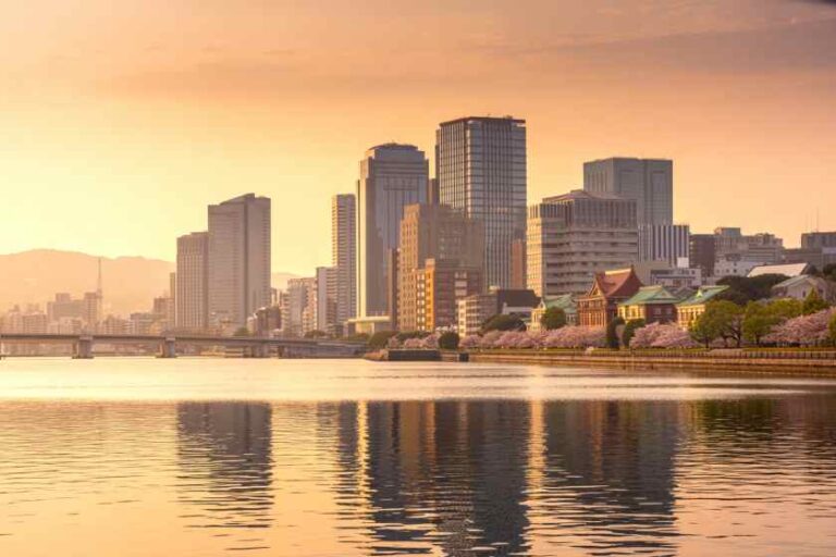 Sunset city skyline along a calm river with reflections of tall buildings on the water.