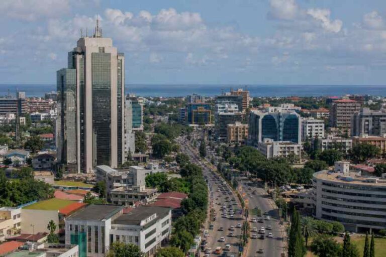 Aerial view of a coastal city with a tall skyscraper, busy avenue, and the sea on the horizon.