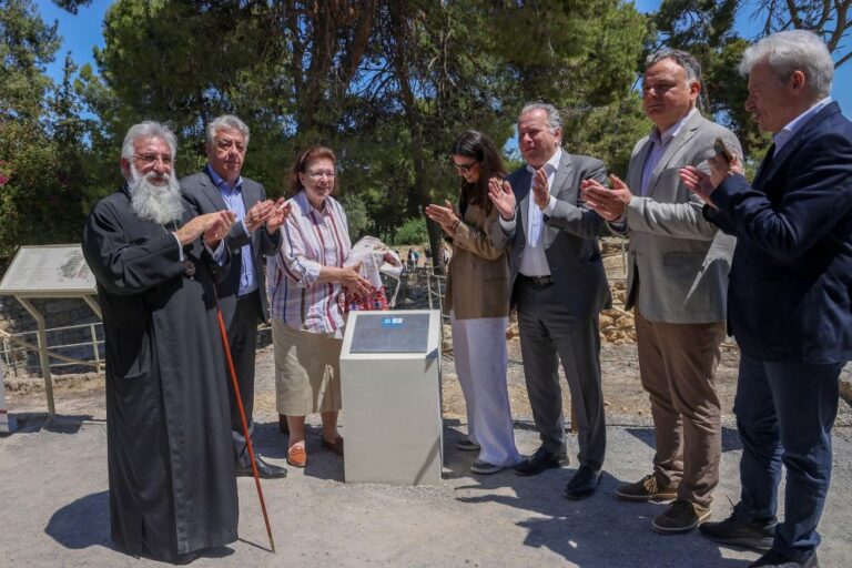 Group of eight adults in a sunny outdoor ceremony clapping around a pedestal plaque.