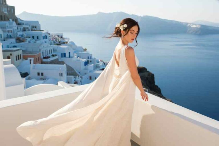 Woman in a flowing white dress on a white terrace, overlooking the blue sea and cliffside village (Santorini).