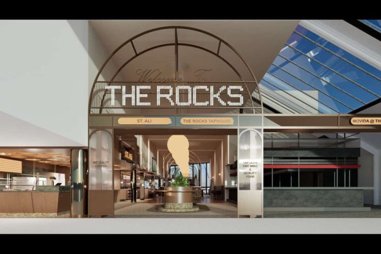 Entrance to a shopping center with a large arch sign reading THE ROCKS and a giant ice cream cone sculpture in a planter center stage.