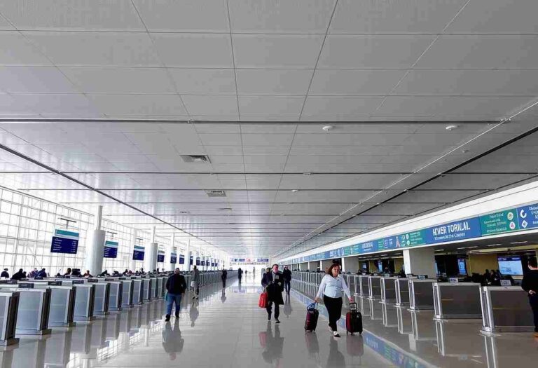Busy airport terminal with travelers and luggage near check-in counters along glass walls and blue signs.