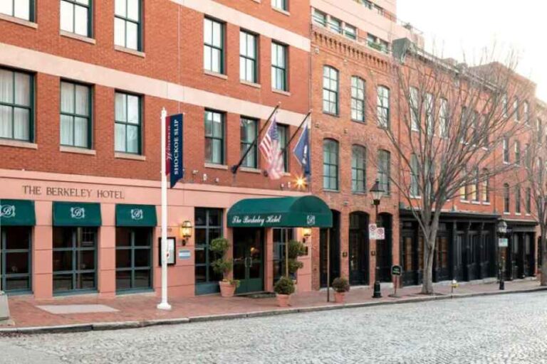 Exterior of The Berkeley Hotel on a cobblestone street; brick building with green awnings, flags, and potted plants.