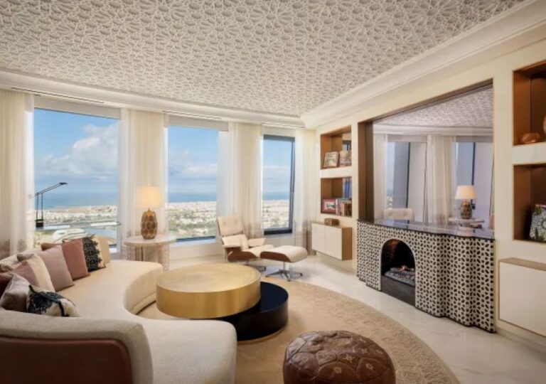 Bright living room with a cream sectional, round gold coffee table, and panoramic ocean view through large windows.
