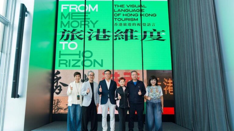 Six adults on a stage giving thumbs up in front of a large green display for a Hong Kong tourism event.
