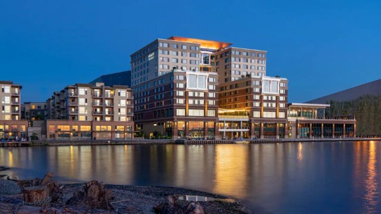 Modern waterfront hotel complex at dusk with warm lights reflecting on calm water.