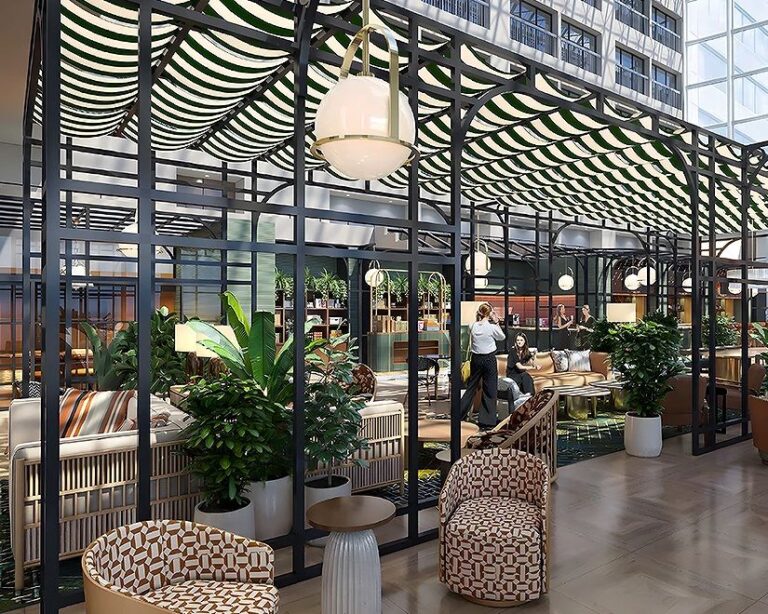 Open, modern lounge with a glass-framed black metal partition, hanging pendant lights, and lush potted plants surrounding patterned seating.
