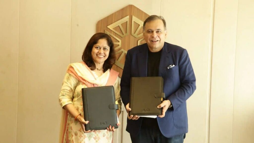 Two professionals, a woman in a floral dress and a man in a dark blazer, smile while holding black folders.