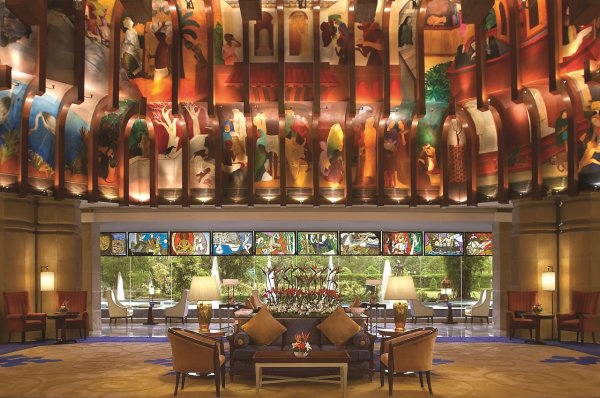 Luxurious hotel lobby with a vibrant suspended art installation overhead and a seating area of sofas and chairs behind glass doors.