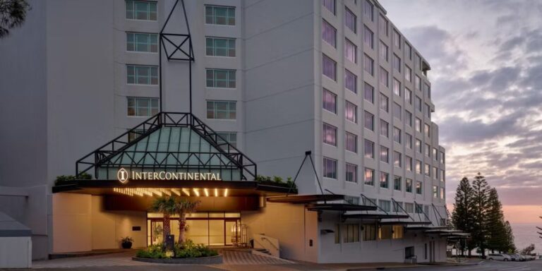 Hotel exterior at sunset with InterContinental sign over a glass porte-cochère and entrance.”] ,