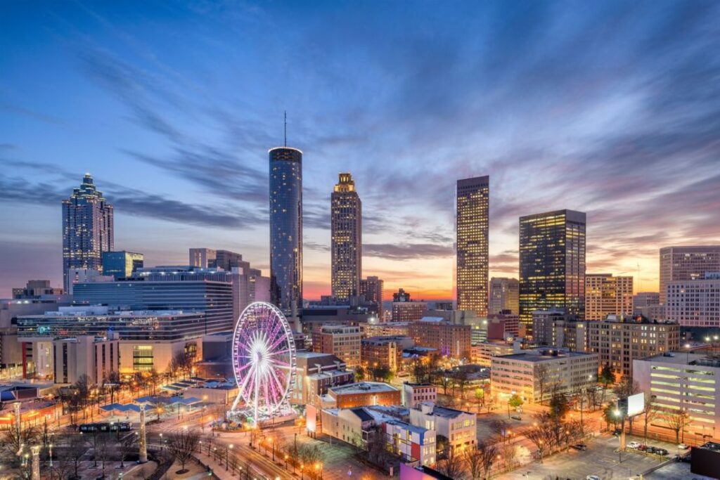 City skyline at dusk with illuminated skyscrapers and a glowing pink Ferris wheel in the foreground.