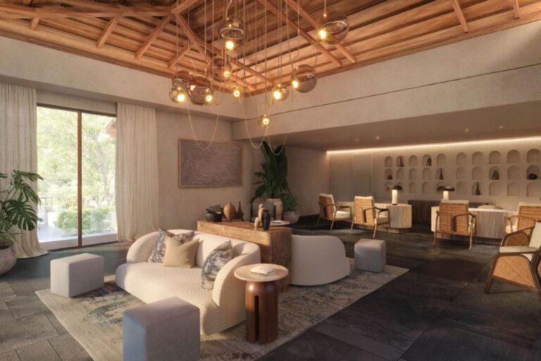 Open-concept living space with a cream sofa, wicker chairs, and warm pendant lights in a high wooden ceiling room with large windows and plants.