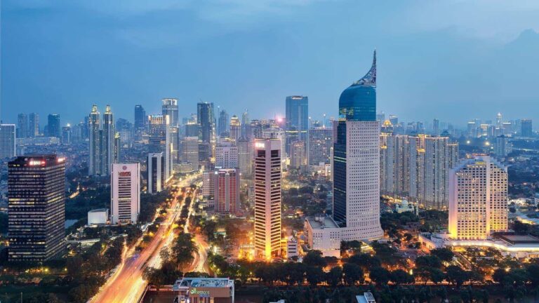 Aerial cityscape featuring a dense cluster of skyscrapers with illuminated streets at dusk.
