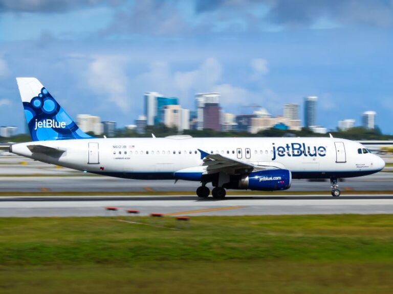 JetBlue airplane taxiing on the runway with a city skyline in the distance.
