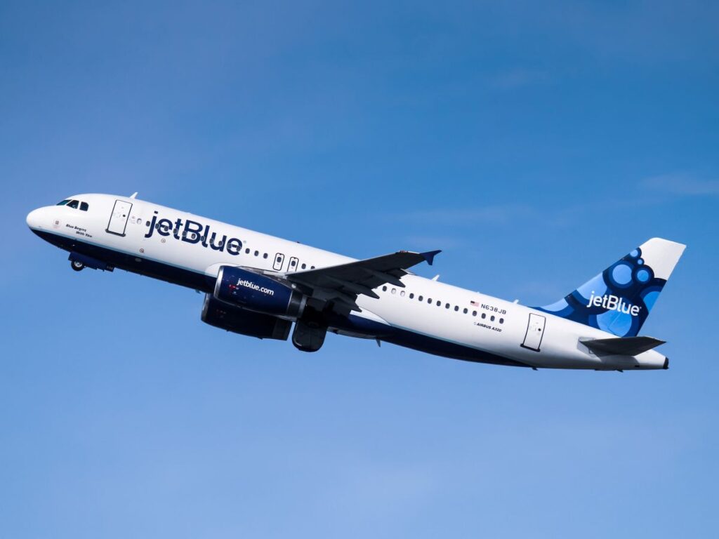 JetBlue Airbus A320 in white and blue livery flying in a clear blue sky.