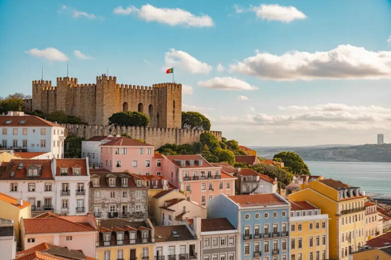 Castle atop a hill overlooking pastel-colored houses by the waterfront under a blue sky.