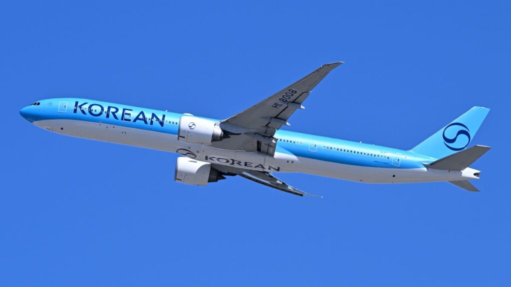 Side view of a Korean Air jet in light blue livery flying against a clear blue sky